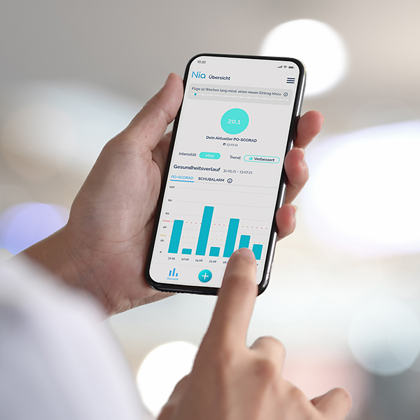 Close up einer Hand mit Smartphone, die Analysebereich der Nia Neurodermitis App geöffnet hat, Finger zeigt auf Analyseauswertung