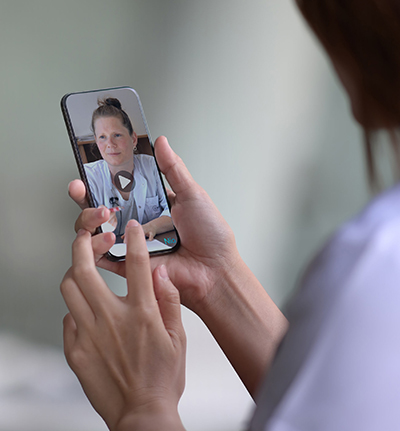 Close up einer Frau, die Smartphone in Hand hält und Video einer medizinischen Expertin betrachtet